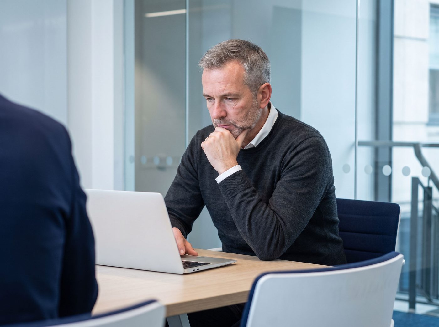 A senior auditor concentrating on his laptop in a glass-walled meeting room